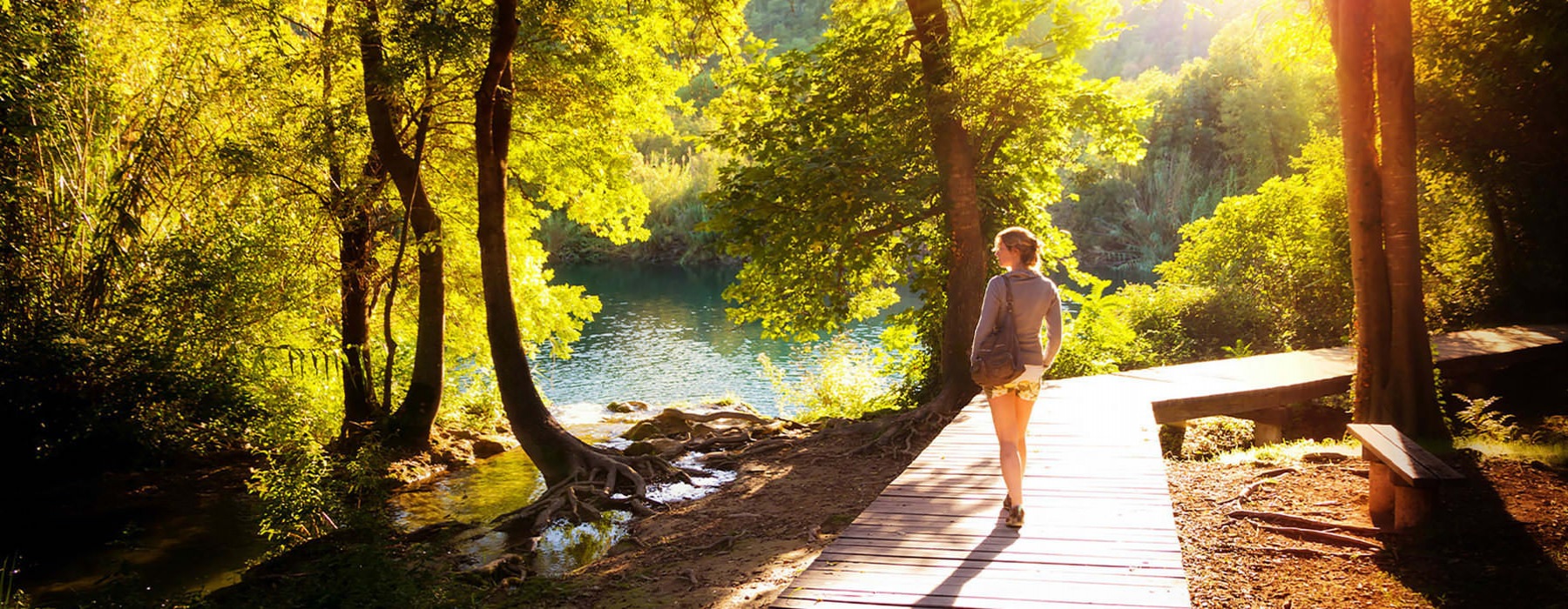 A women is walking down a beautiful wooded path alongside a river.